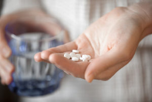 Person about to take white pills with a glass of water