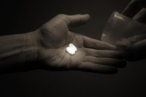 A dimly lit hand holding two white pills
