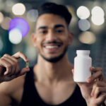 Fitness Supplements. Sporty Middle Eastern Guy Demonstrating Blank White Jar And Capsule Pill, Arab Male Athlete Advertising Multivitamins For Sports And Bisybuilding, Selective Focus, Closeup