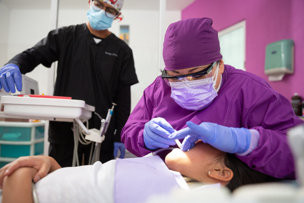 A Mexican female dentist doing dental treatment on a young girl with the male assistant helping her