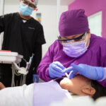 A Mexican female dentist doing dental treatment on a young girl with the male assistant helping her