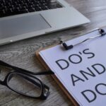 Laptop, glasses and paper clipboard with text DO'S AND DON'TS on table.