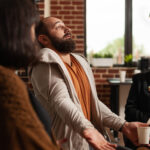 Close up of man sharing addiction issues with aa meeting group and therapist. Person explaining anxiety and depression problems at support therapy with psychiatrist sitting in circle.
