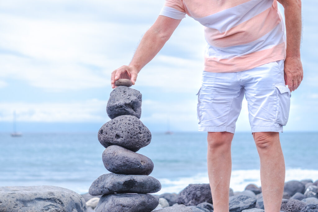 Stones tower on the coast of the sea in the nature. Ocean beach, six pebbles tower. Caucasian man put the last piece. Concept of balance and harmony.