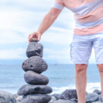 Stones tower on the coast of the sea in the nature. Ocean beach, six pebbles tower. Caucasian man put the last piece. Concept of balance and harmony.