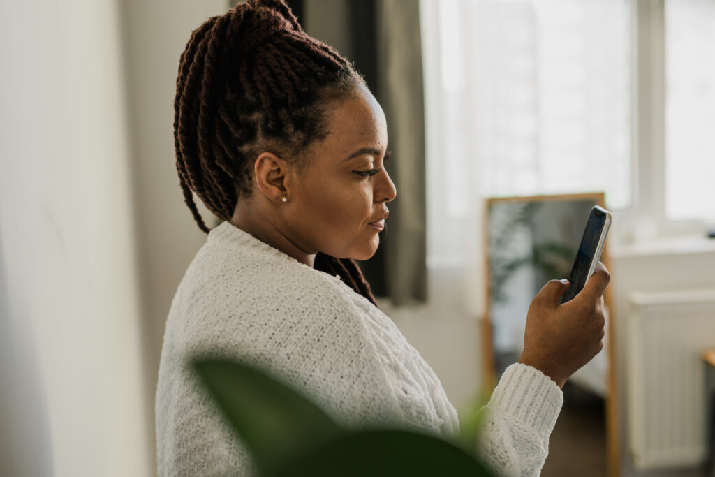 Portrait of good-looking African female student dressed casually holding mobile phone and typing messages and communicating with friends social networks using high-Internet connection.