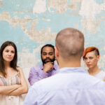 Young man speaks to other young people by grunge wall