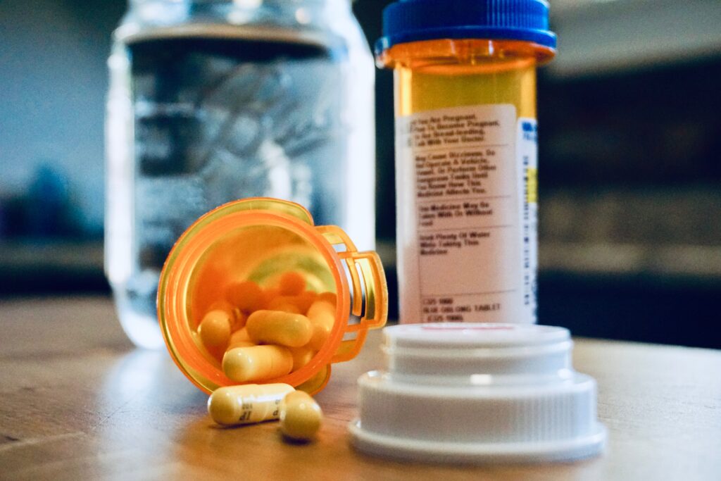 bottle-of-spilled-pills-with-glass-of-water-in-bac-2024-12-06-11-08-07-utc