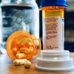 bottle-of-spilled-pills-with-glass-of-water-in-bac-2024-12-06-11-08-07-utc