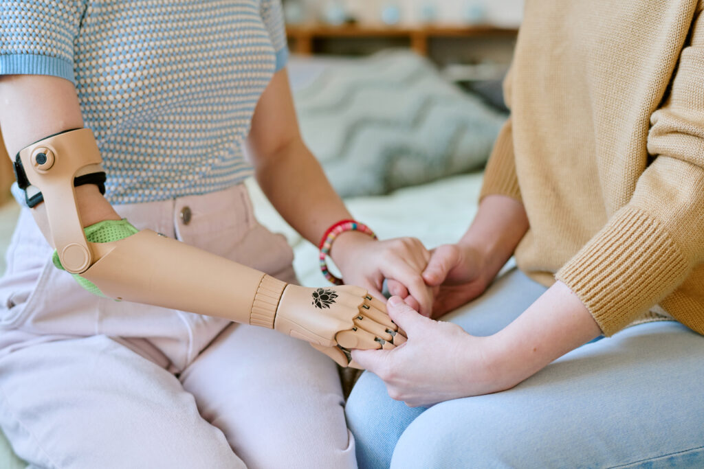Close view of two individuals sitting close together, one with prosthetic arm, holding hands and sharing moment of support and connection