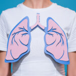 partial view of woman in white tshirt with paper crafted lungs on blue backdrop