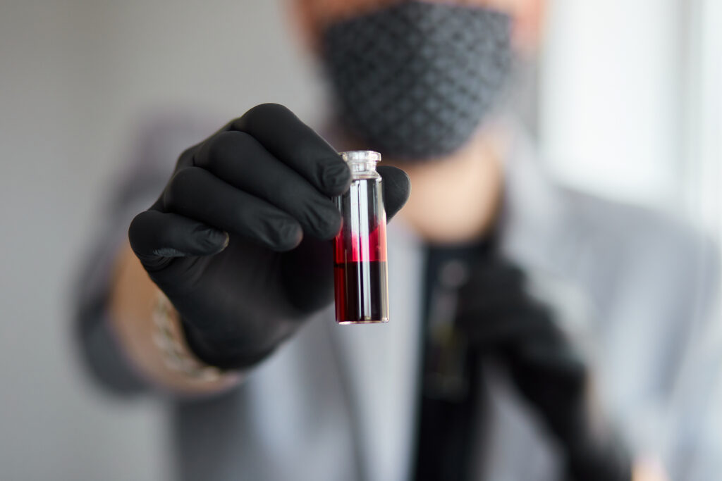 Young man holding test tubes with blood and antidote in his hand. Coronavirus blood Test tube. Positive Blood Sample in Scientist Hand.