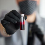 Young man holding test tubes with blood and antidote in his hand. Coronavirus blood Test tube. Positive Blood Sample in Scientist Hand.